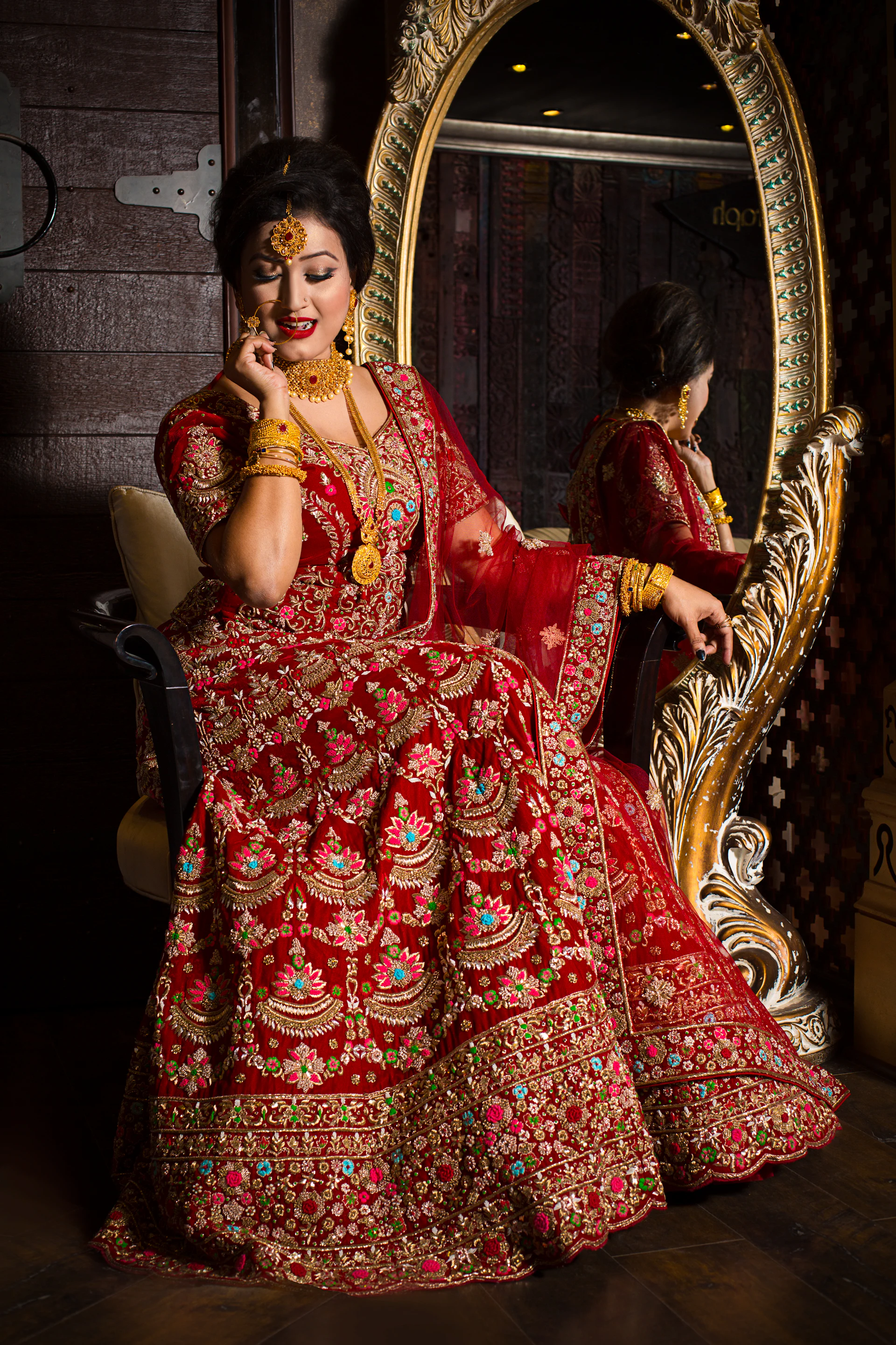 Bride in red and gold lehenga seated on a carved armchair