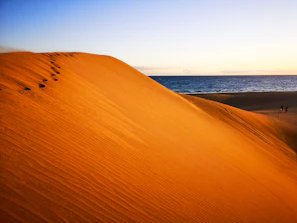 Golden sand dunes meeting the Atlantic Ocean with footprints leading into the distance