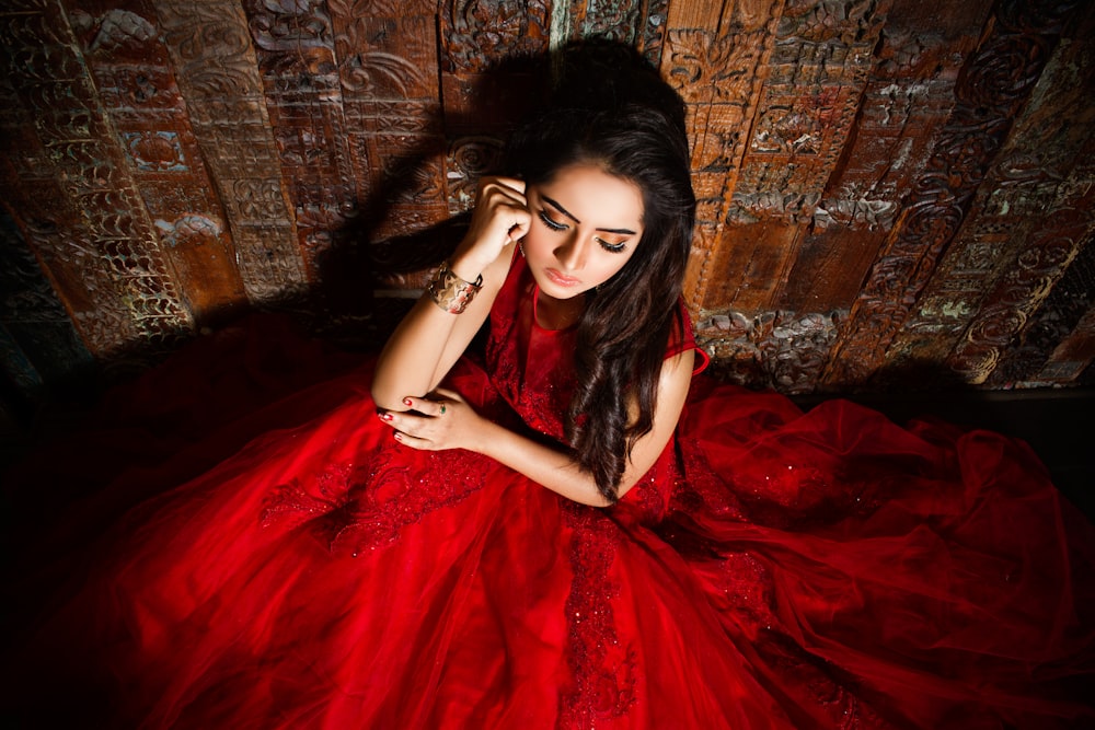 woman in red dress leaning on brown wall