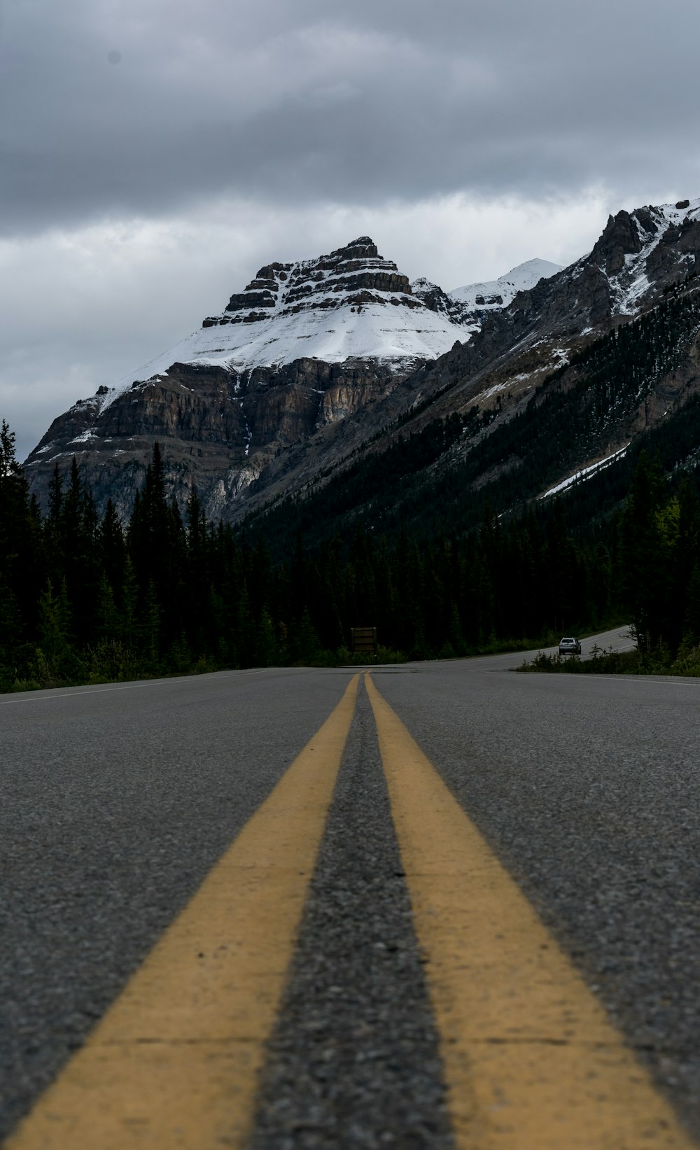 gray concrete road near green trees and snow covered mountain during daytime