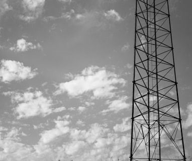 grayscale photo of electric tower under cloudy sky