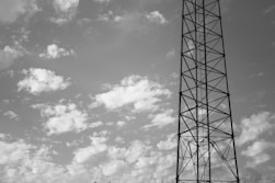 grayscale photo of electric tower under cloudy sky