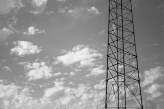 grayscale photo of electric tower under cloudy sky