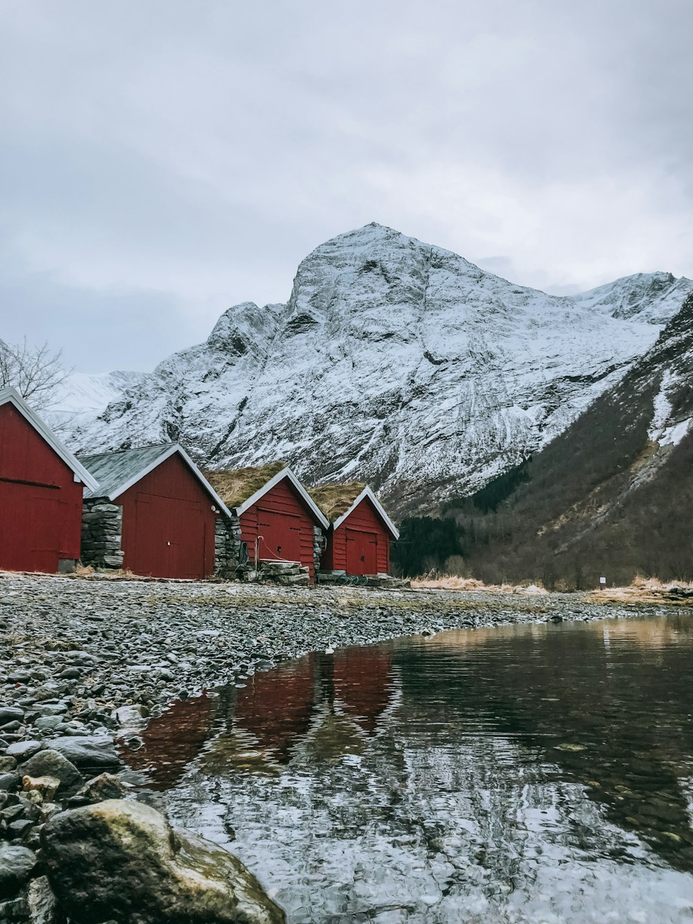 red and white wooden house near body of water and gray rocky mountain during daytime