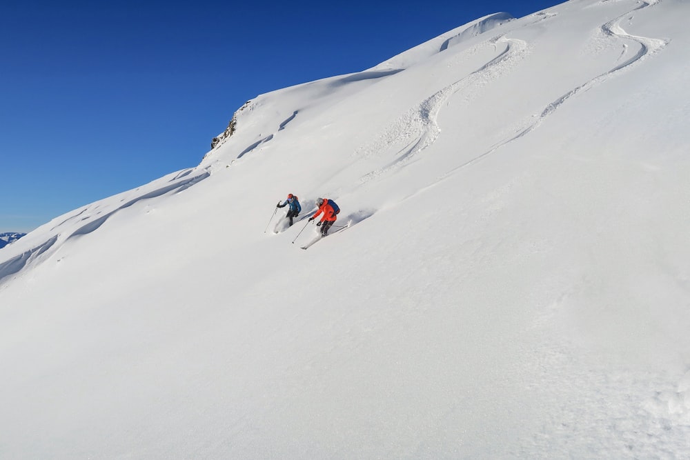 昼間の雪山で赤いジャケットと青いズボンを着た人