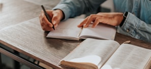 person in gray long sleeve shirt holding black pen writing on white paper