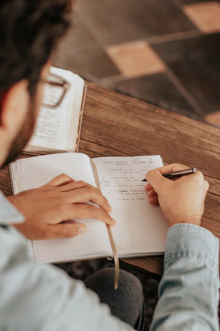 A thoughtful person writing notes while reading economic reports in a modern office.
