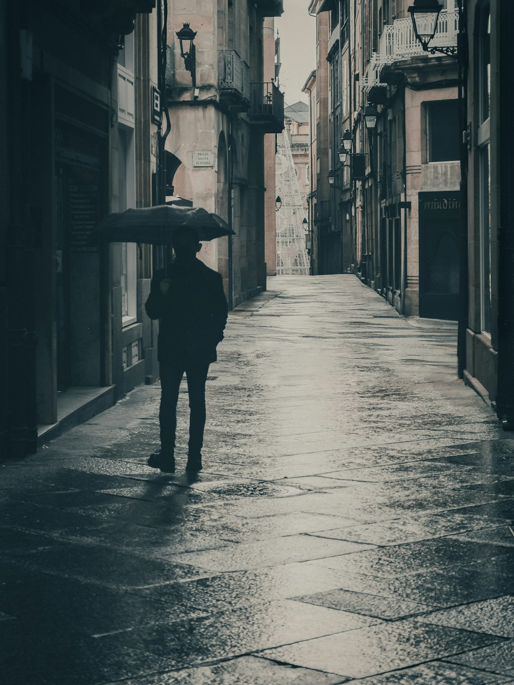 Person in schwarzer Jacke mit Regenschirm geht tagsüber auf der Straße