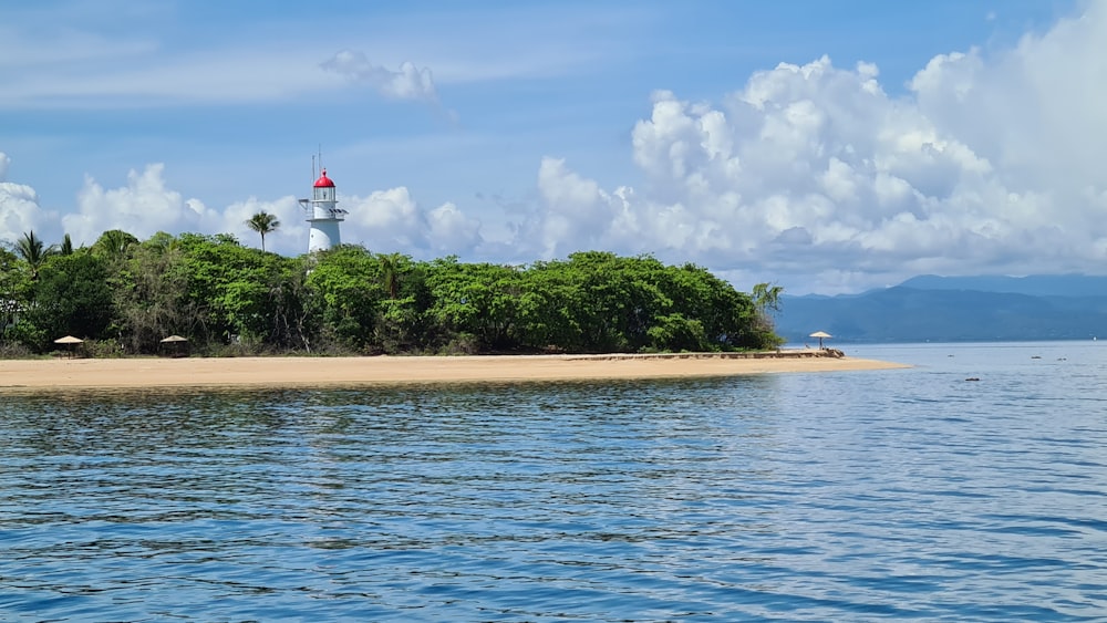 white and red lighthouse near green trees and body of water under blue and white cloudy