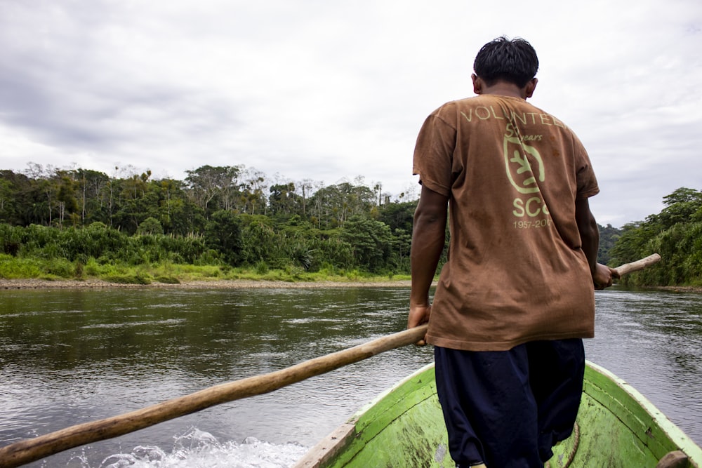 man in brown shirt and blue pants standing on green boat during daytime