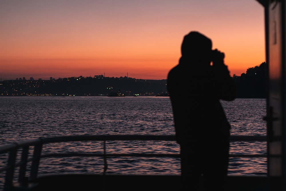 silhouette of man standing near body of water during sunset