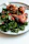 Close-up of a colorful plate with roasted chicken and fresh sides on a rustic wooden table.