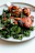 Close-up of a colorful plate with roasted chicken and fresh sides on a rustic wooden table.
