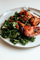 A plate of roasted chicken served on a bed of fresh kale, garnished with sprigs of thyme and scattered pomegranate seeds.