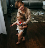 girl in brown long sleeve shirt and white shorts sitting on brown wooden floor