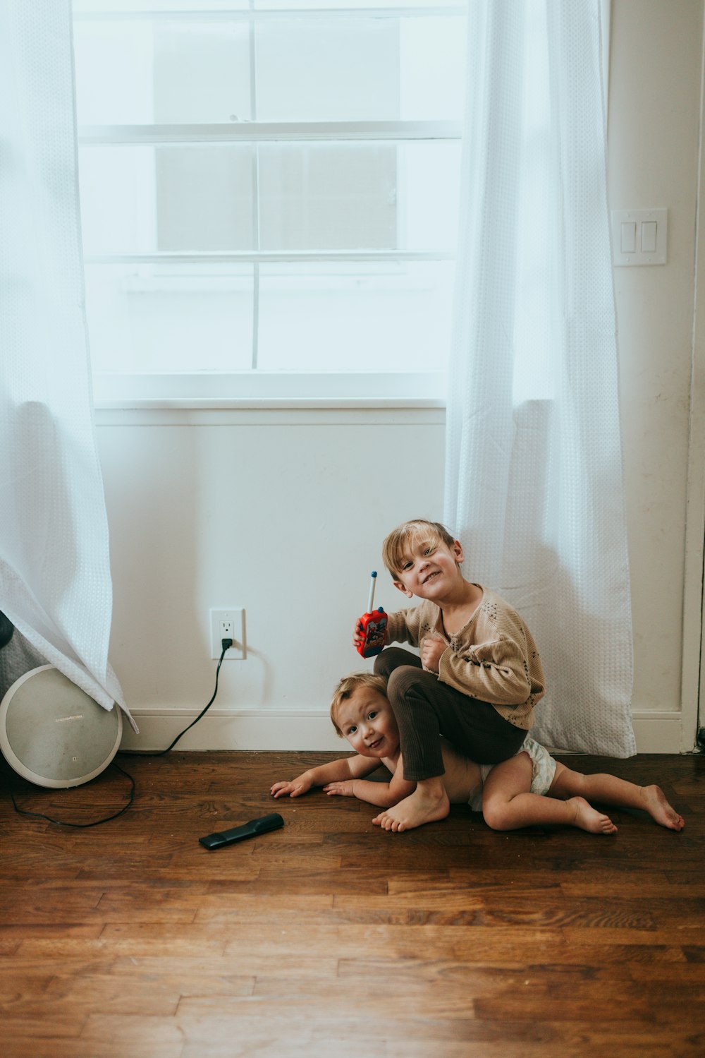 woman in brown long sleeve shirt sitting on floor with baby in white long sleeve shirt