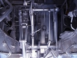 A complex arrangement of mechanical parts and components, including metal rods, pipes, and various interconnected structures. The image displays an intricate assembly of machinery with a metallic sheen and various textures, indicative of industrial engineering.