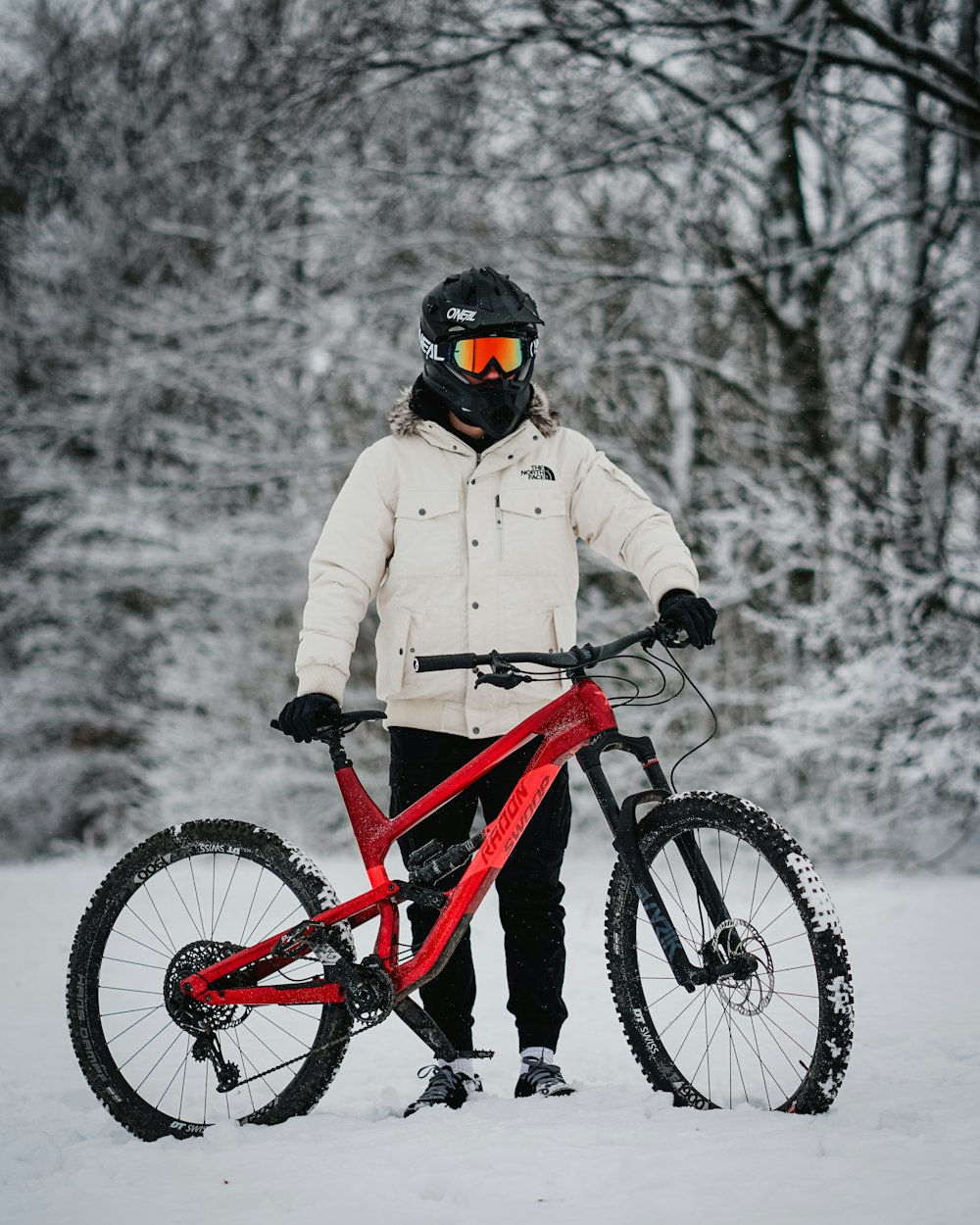 man in beige jacket riding red mountain bike on snow covered ground during daytime