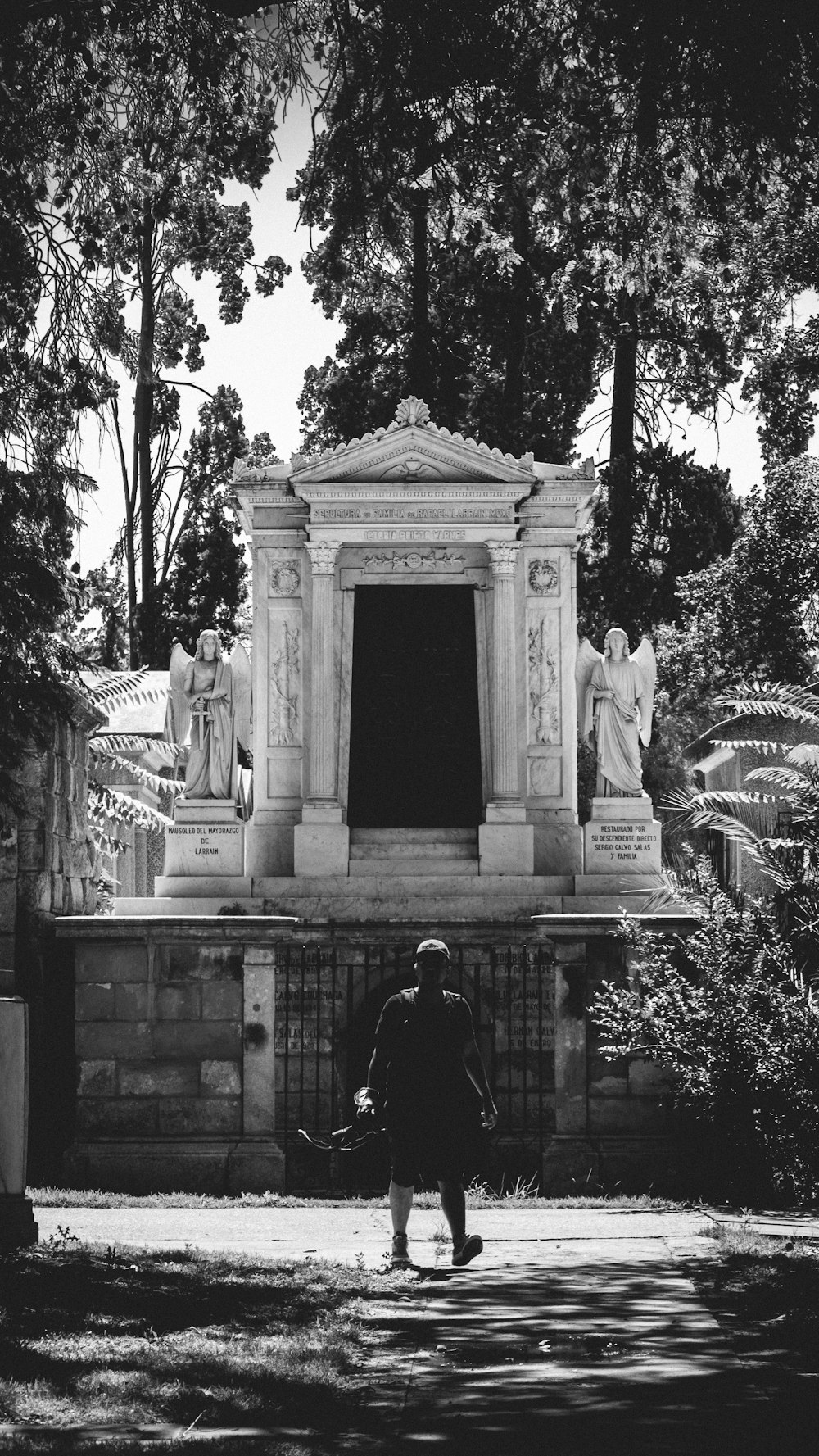 grayscale photo of man in black jacket standing in front of statue