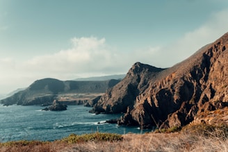brown mountain beside body of water during daytime