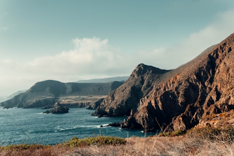 brown mountain beside body of water during daytime