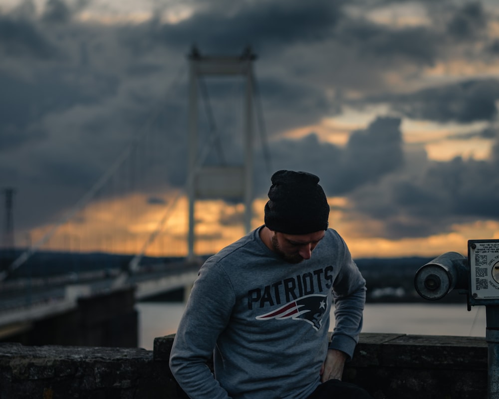 man in gray and white pullover hoodie and black knit cap sitting on brown wooden bench