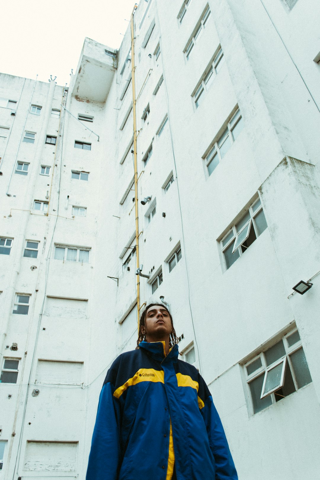 man in blue and yellow jacket standing near white concrete building during daytime