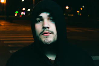 Model wearing a black hoodie with orange accents, standing under urban street lights at dusk