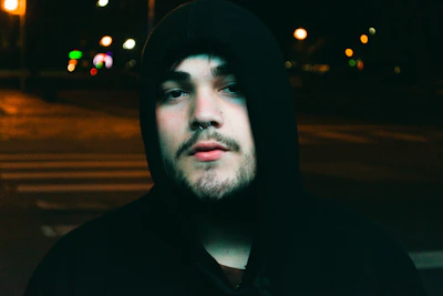 Model wearing a black hoodie with orange accents, standing under urban street lights at dusk