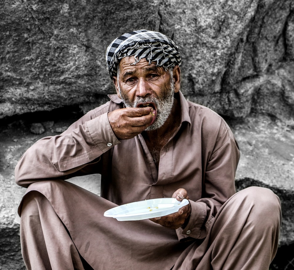 man in brown thobe sitting on gray concrete floor