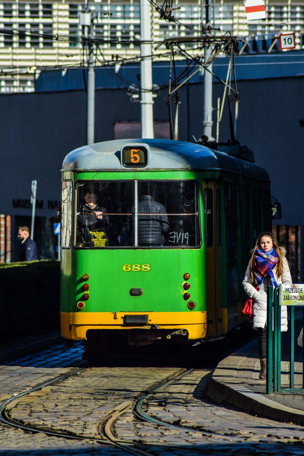 Femme en veste blanche debout à côté du tramway jaune et blanc pendant la journée