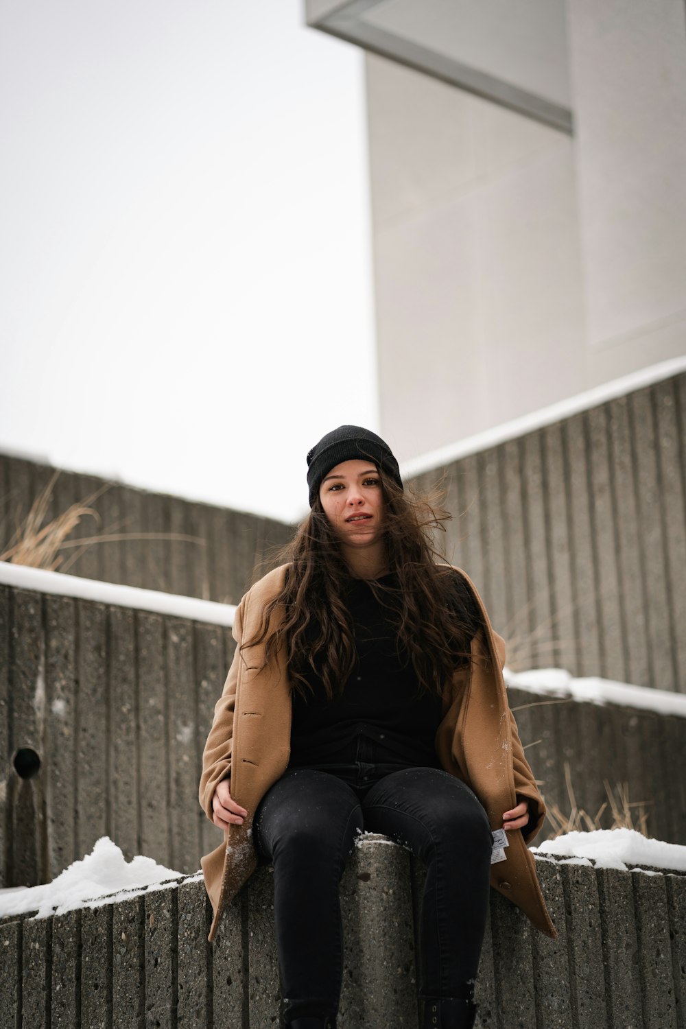 woman in black knit cap and brown long sleeve shirt sitting on white textile during daytime