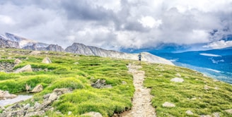 green grass field near mountain under white clouds during daytime