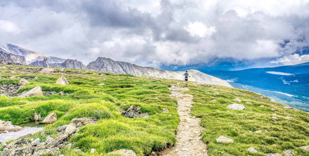 green grass field near mountain under white clouds during daytime