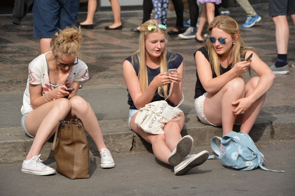 3 mulheres sentadas no chão de concreto cinza durante o dia
