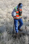 man in orange and black backpack and blue denim jeans standing on brown grass field during