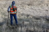 man in orange and black jacket and blue denim jeans standing on brown grass field during