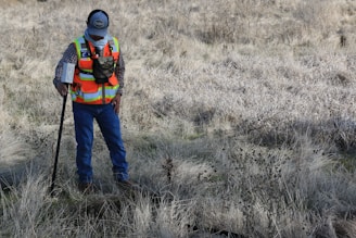 man in orange and black jacket and blue denim jeans standing on brown grass field during