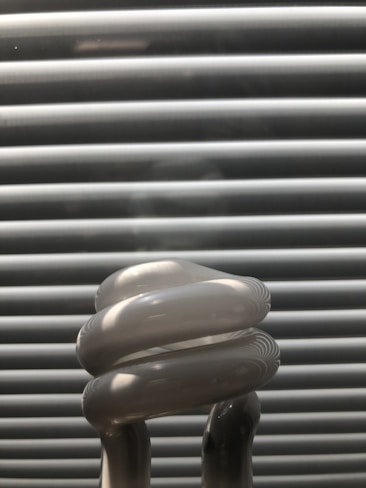 A close-up view of a compact fluorescent light bulb with a spiral shape set against a background of horizontal blinds.