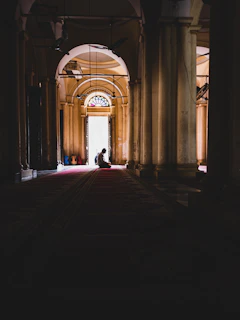 Sunlight streaming through chapel arches onto a kneeling worshipper deep in reflection