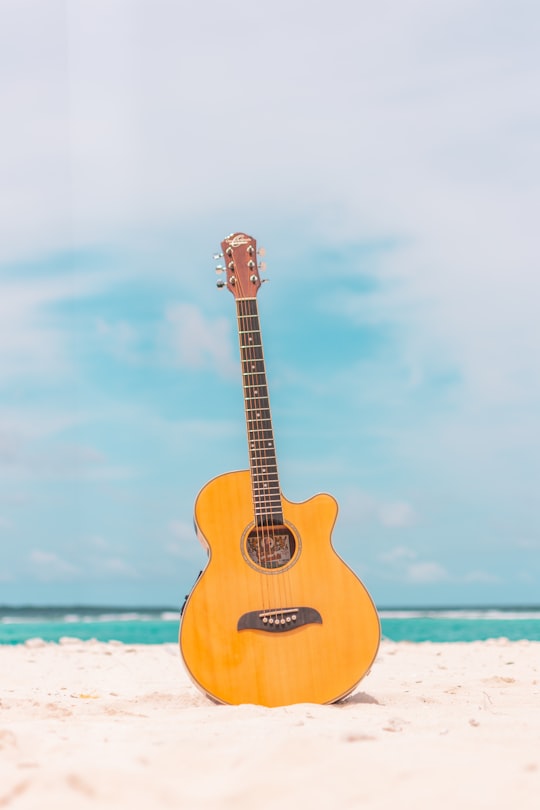 brown acoustic guitar on white sand during daytime in Kulhudhuffushi Maldives