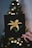 A hand holds a black card featuring a yellow lily with green leaves. In the background, there are blurred lights resembling a softly focused Christmas tree adorned with yellow and white bokeh lights.