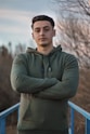 man in green hoodie standing on blue metal railings during daytime