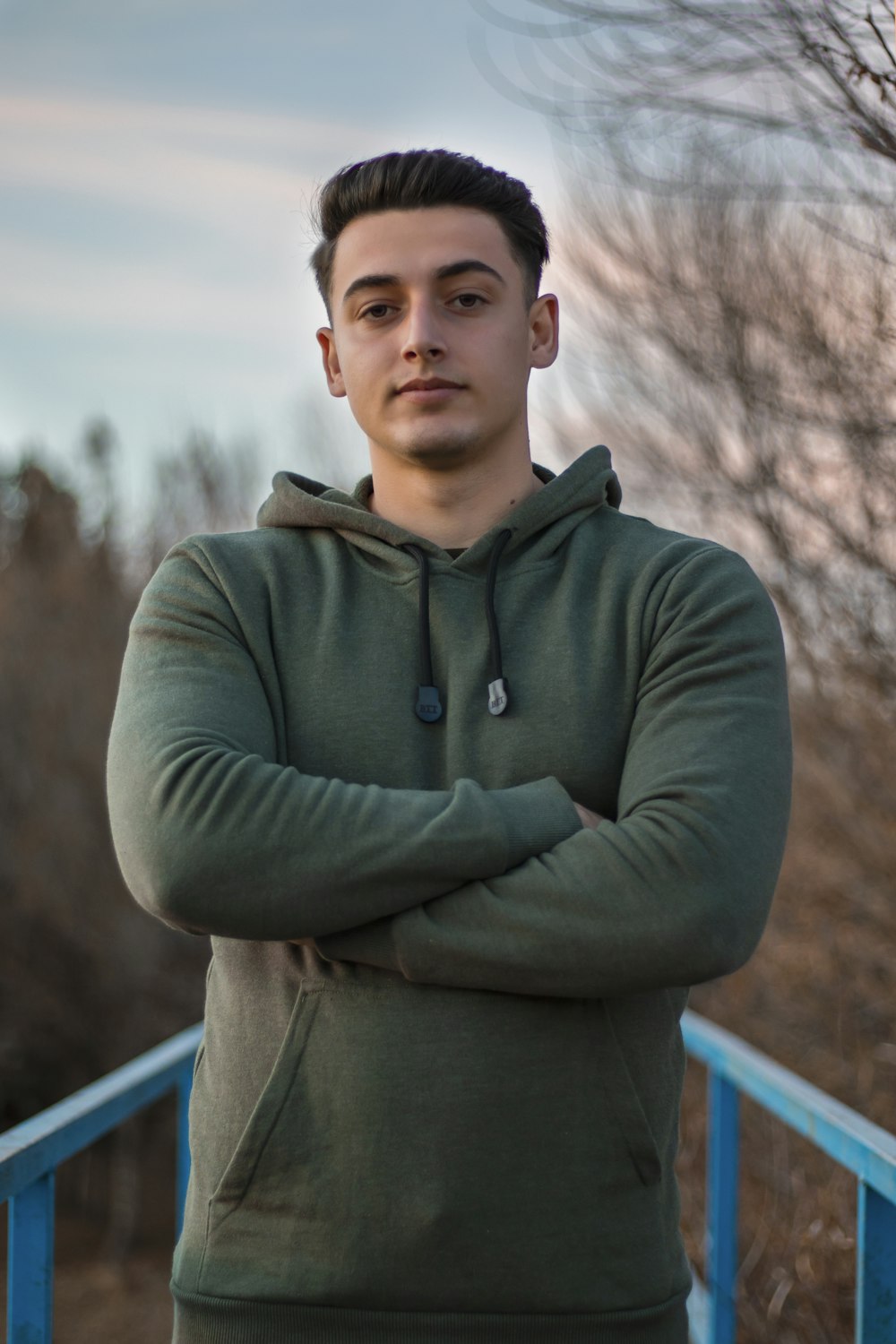 man in green hoodie standing on blue metal railings during daytime