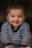 A smiling baby dressed in a striped sweater, captured against a soft, dark background. The baby's joyful expression is emphasized by its chubby cheeks and sparkling eyes.