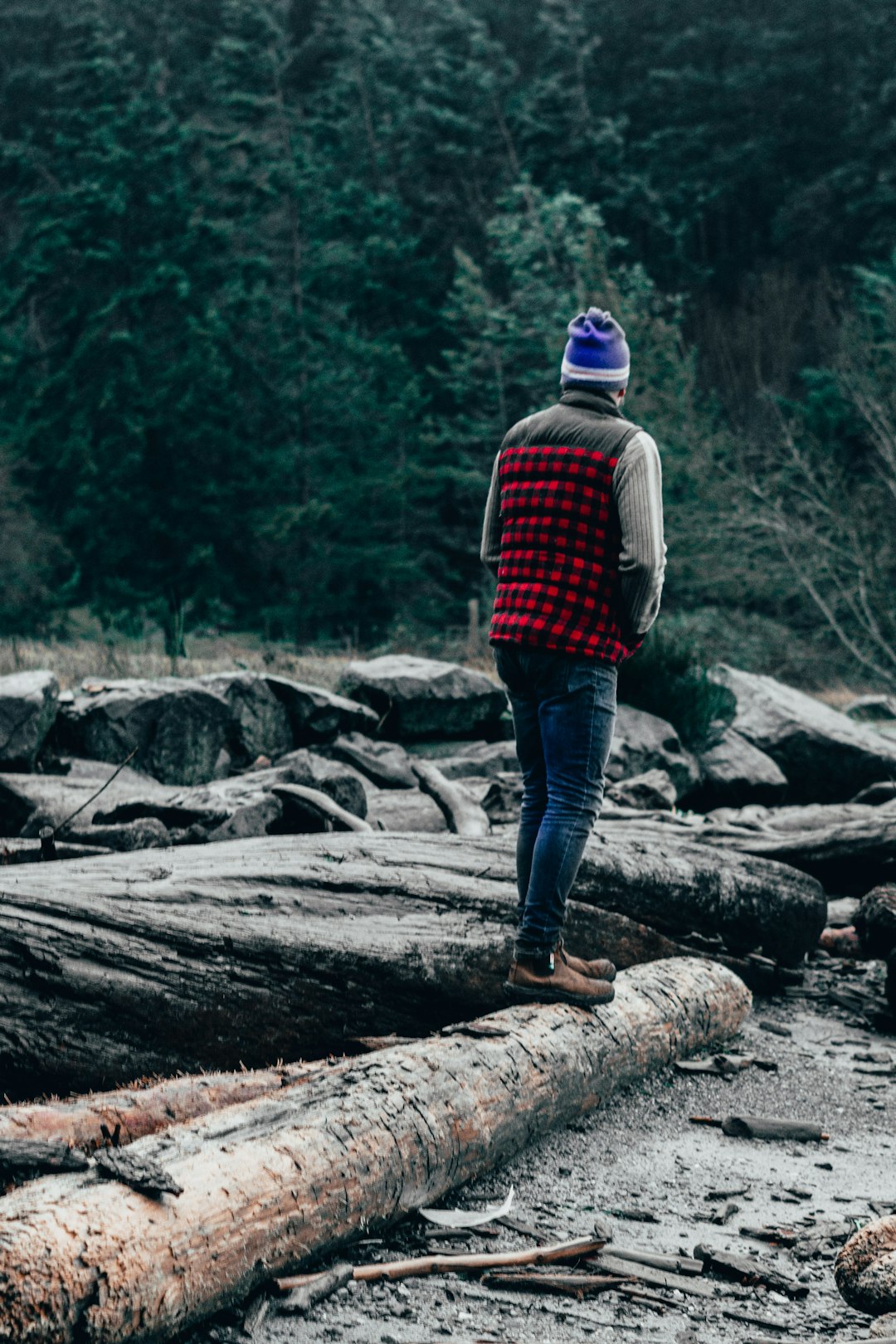 man in red and black plaid dress shirt and blue denim jeans standing on brown rock