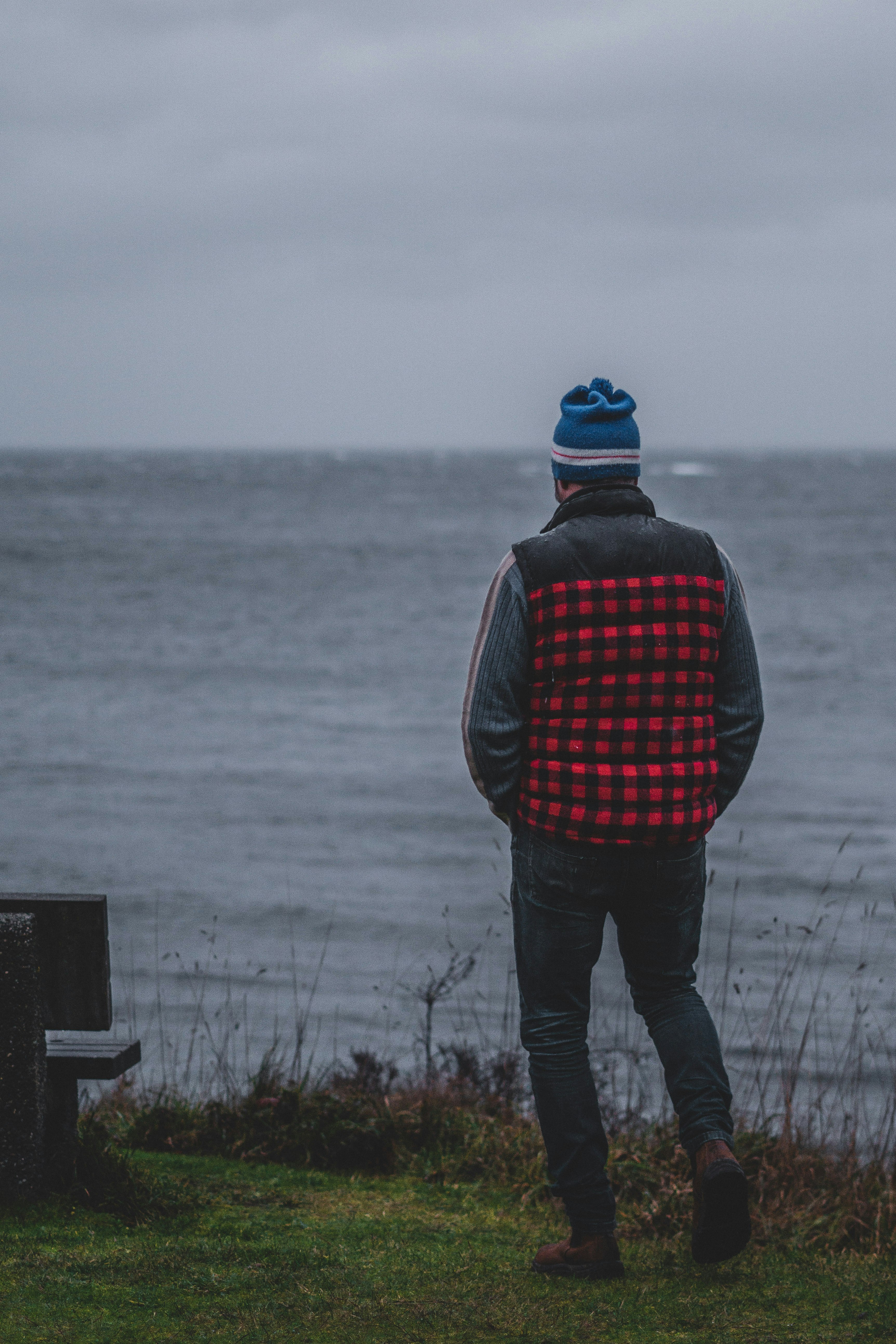 man in black and red plaid jacket and black pants standing on seashore during daytime