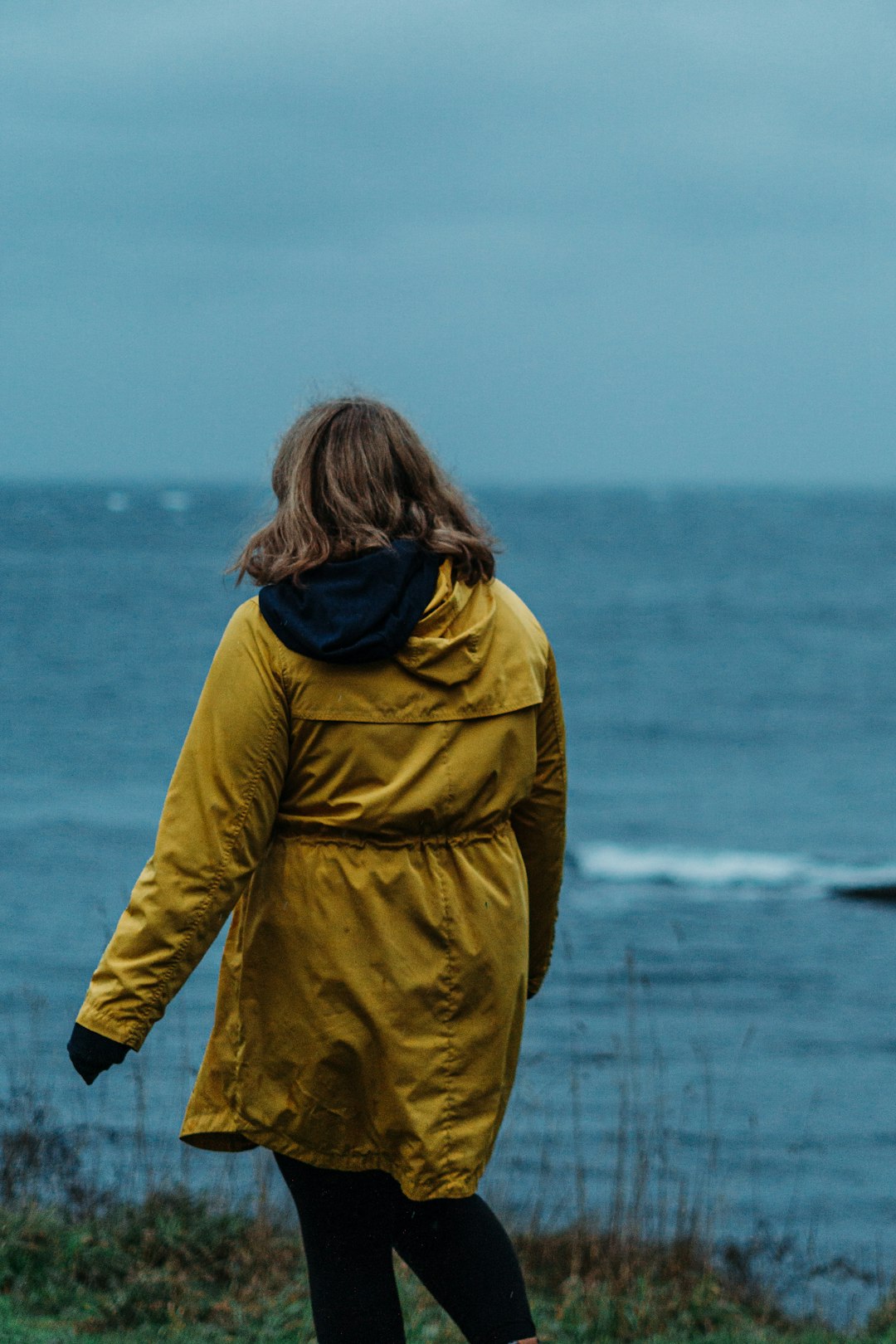 woman in yellow hoodie standing near body of water during daytime