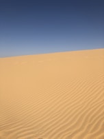 Golden sand dunes stretching endlessly under a bright blue desert sky.