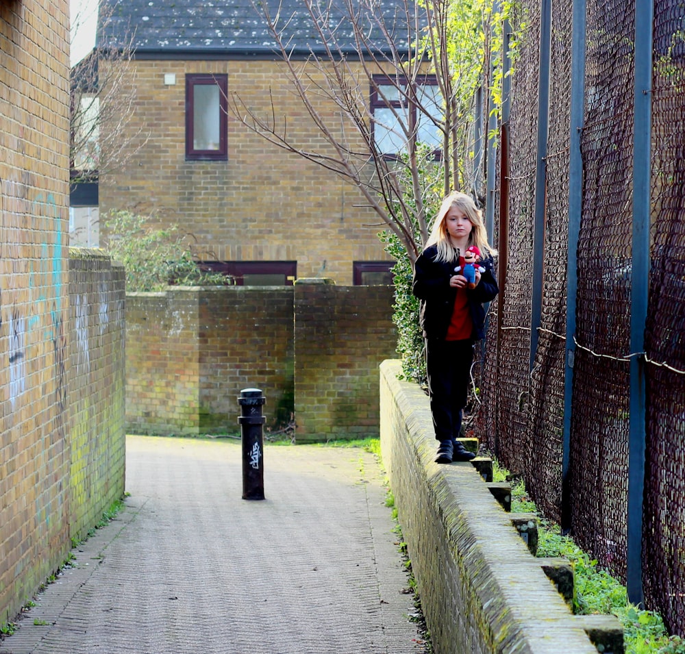 Mujer con chaqueta negra de pie en un camino de hormigón gris cerca de un edificio de ladrillo marrón durante el día